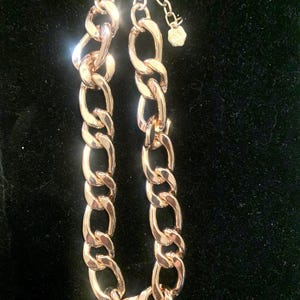 May include: Gold-toned chain necklace with large, interlocking links. The necklace has a lobster clasp closure and an adjustable chain. The chain is displayed against a dark background.