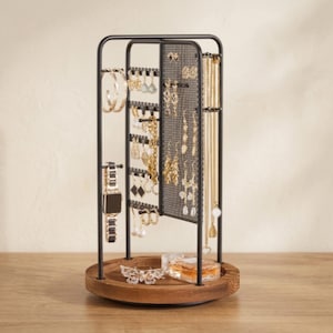 May include: A rotating jewelry organizer featuring a black metal frame with a mesh panel for earrings and hooks for necklaces and bracelets. The stand is mounted on a circular wooden base that holds a small glass perfume bottle and a butterfly ornament.