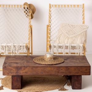 Può includere: Una scena di soggiorno rustica con un tavolino in legno marrone scuro, due sedie in macramè e un paravento in vimini. Un cappello di paglia è appeso a una sedia. Un cuscino decorativo in macramè e una candela sono sul tavolo.