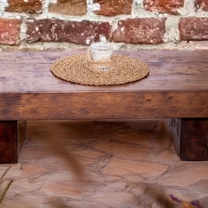May include: A dark brown wooden coffee table with a rectangular top and four square legs. A woven placemat and a glass jar sit on the table. The table is set against a brick wall. The table's dimensions are approximately 120 cm long.