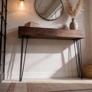 Puede incluir: Una consola de madera marr&oacute;n oscuro con patas de horquilla negras. Un espejo redondo negro cuelga sobre la mesa y un jarr&oacute;n con plantas secas est&aacute; sobre la mesa. Una l&aacute;mpara cuelga del techo.