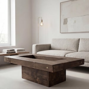 Könnte beinhalten: Ein dunkelbrauner rechteckiger Couchtisch mit einer vertieften Mitte. Der Tisch ist aus Holz gefertigt und hat einen soliden Sockel. Der Raum hat eine neutrale Farbpalette mit einem Sofa und einer Stehlampe.