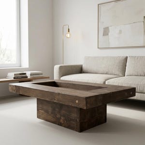 Peut inclure: Une table basse rectangulaire marron foncé avec un centre en retrait. La table est en bois massif et présente un design simple et moderne. La table mesure environ 122 cm de long, 61 cm de large et 41 cm de haut.