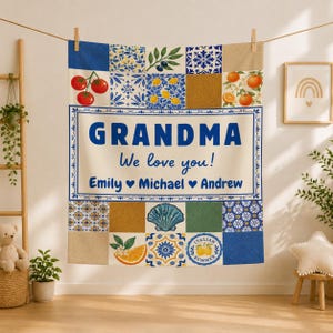 May include: A rectangular throw blanket featuring a patchwork design of blue and white Mediterranean-style tiles, citrus fruits, tomatoes, and a seashell. The center text reads: GRANDMA We love you! Emily ♥ Michael ♥ Andrew.