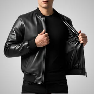 May include: A black leather bomber jacket with a ribbed collar, cuffs, and hem. The jacket has a zip-up front and two side pockets. The interior lining is black. The model is wearing a black shirt underneath.