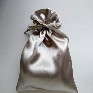May include: A light gray satin drawstring bag with a gathered top and a tied ribbon.