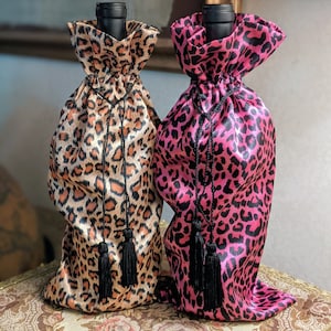 May include: Two wine bottle gift bags with leopard print designs. One bag is brown and black, the other is pink and black.