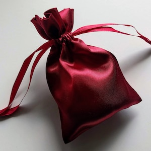 May include: A red satin drawstring bag with a gathered top and a long, thin cord.