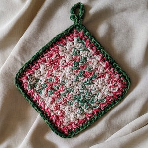 May include: A crocheted pot holder with a green and pink pattern. The pot holder has a loop for hanging.