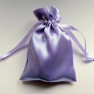 May include: A lavender satin drawstring bag. The bag is made of soft, silky fabric and has a gathered top with a drawstring closure.