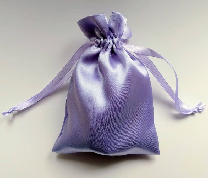 May include: A lavender satin drawstring bag. The bag is made of soft, silky fabric and has a gathered top with a drawstring closure.