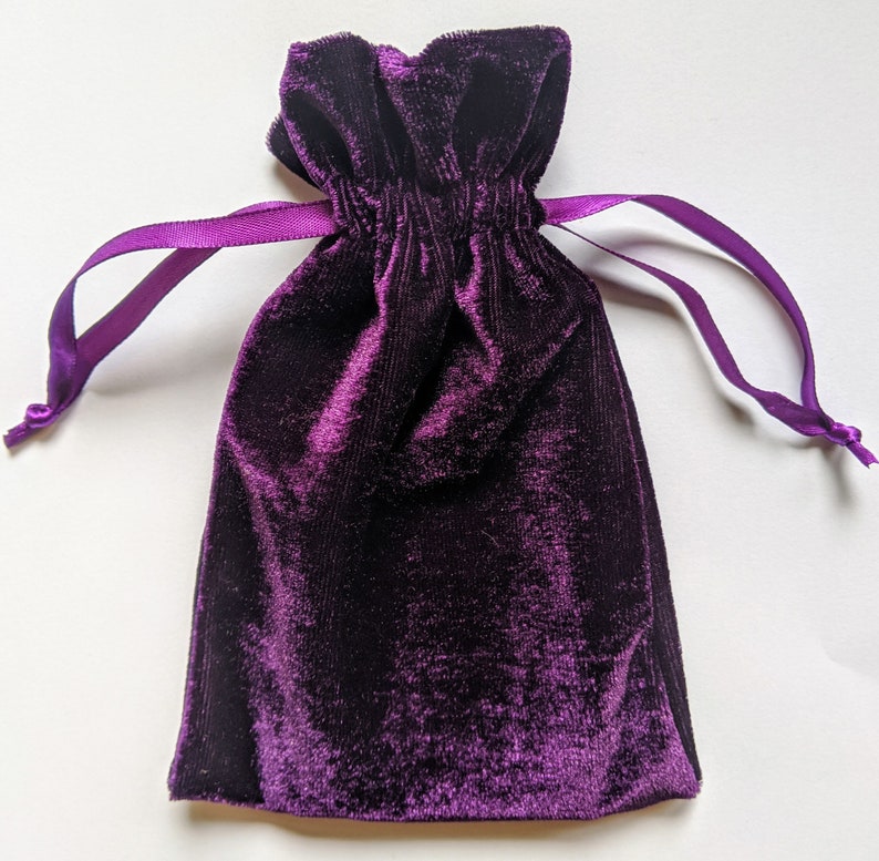 May include: A purple velvet drawstring bag with a gathered top. The bag is made of soft, plush velvet and has a silky feel.