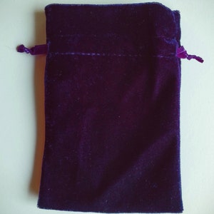 May include: A small, dark purple velvet pouch with a drawstring closure. The pouch is made of soft, plush fabric and has a smooth, even texture.