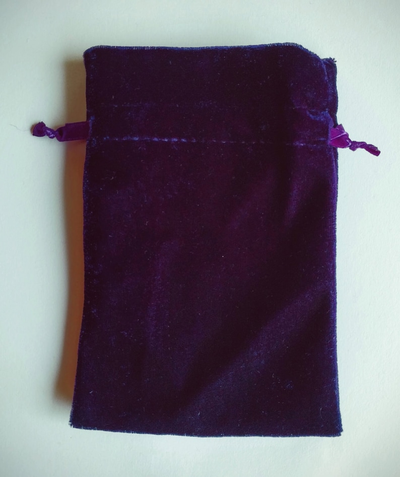May include: A small, dark purple velvet pouch with a drawstring closure. The pouch is made of soft, plush fabric and has a smooth, even texture.