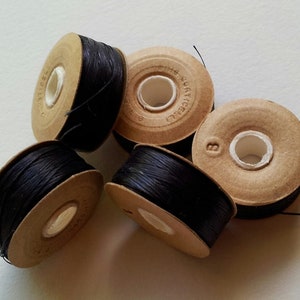 May include: Four spools of black thread wound around cardboard spools. The spools are labelled "Richelli" and "B".