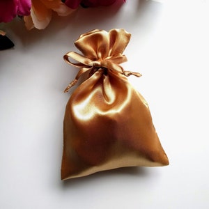 May include: A gold satin drawstring bag with a bow. The bag is empty and ready to be filled with a gift.