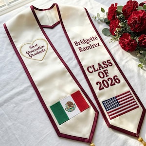 May include: Ivory graduation sash with burgundy trim, featuring the text "First Generation Graduate" in a heart, the name "Bridgette Ramirez", and "CLASS OF 2026". Includes Mexican and American flags. A bouquet of red flowers is in the background.