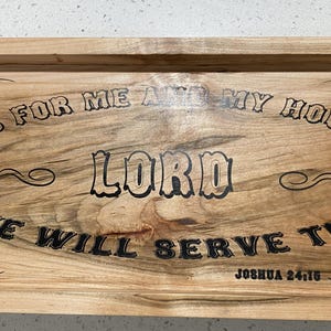 Könnte beinhalten: Serviertablett aus Holz mit Griffen, mit dem eingravierten Text "AS FOR ME AND MY HOUSE WE WILL SERVE THE LORD" und dem Bibelvers Josua 24,15. Das Tablett hat eine natürliche Holzmaserung.