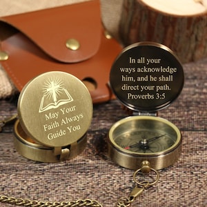 May include: Two antique brass compasses with inspirational quotes engraved on the lids. One reads "May Your Faith Always Guide You" and the other "In all your ways acknowledge him, and he shall direct your path. Proverbs 3:5". A brown leather case is in the background.