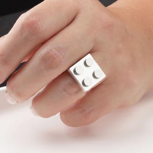 May include: A silver ring with a square design, featuring four circular studs. The ring is a unique accessory, perfect for those who appreciate modern and geometric jewelry. The ring is a statement piece.