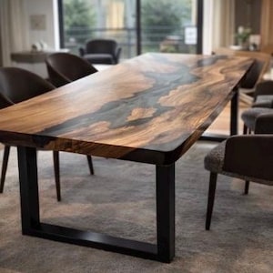 Op de afbeelding: Een grote, rechthoekige houten eettafel met een donkere epoxy rivier in het midden. De tafel heeft een natuurlijke houtnerf afwerking en staat op zwarte metalen poten. De tafel is ongeveer 244 cm lang.