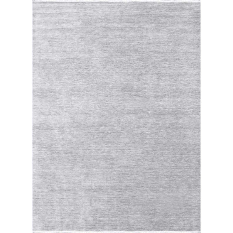 May include: A rectangular, light gray rug with a textured surface. The rug has a subtle, horizontal pattern and a soft, neutral color palette, suitable for various interior design styles. The rug's edges are finished with a thin, white border.