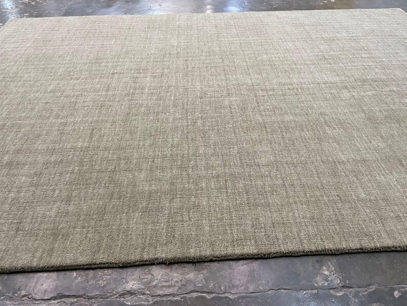 May include: A large, rectangular area rug in a neutral, light green color. The rug has a textured surface with a subtle, linear pattern. The rug is suitable for a living room or bedroom.