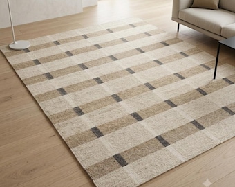 May include: A rectangular area rug featuring a repeating grid pattern of horizontal and vertical bands in shades of beige, tan, and dark charcoal grey. The rug has a textured, woven appearance with a consistent colour palette throughout the design.