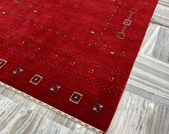 May include: A striking red rug with a geometric design. The rug has a solid red central area, decorated with rows of small, colourful shapes and rectangular borders. The edges are finished with a cream-coloured border.