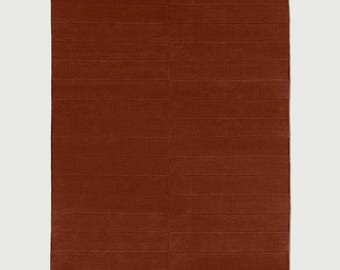 Puede incluir: Una alfombra rectangular de color naranja óxido profundo y sólido. La alfombra presenta una serie de líneas horizontales y paralelas cosidas que recorren toda la superficie, creando una textura sutil en forma de cuadrícula en la tela.