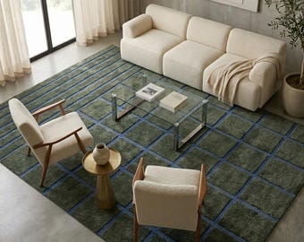 Puede incluir: Una alfombra rectangular grande con un patrón de cuadrícula verde oliva oscuro con líneas azules, colocada debajo de un sofá de tres plazas color crema, dos sillones color crema con marcos de madera, una mesa de centro de cristal y una mesa auxiliar dorada.