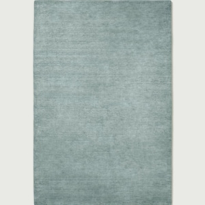 May include: A rectangular area rug in a solid, muted sage green colour. The surface features a subtle, horizontal linear texture that runs across the entire length of the rug, creating a soft, uniform appearance with slight variations in tone.
