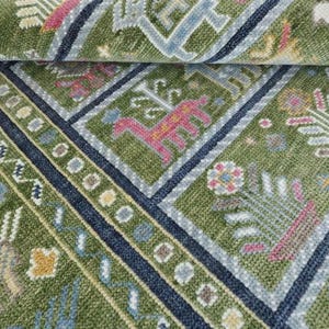 Könnte beinhalten: Nahaufnahme eines grün-blauen gemusterten Teppichs. Der Teppich weist geometrische Formen und florale Motive in Rosa-, Gelb- und Blautönen auf. Der Teppich ist oben aufgerollt und gibt die Unterseite frei.