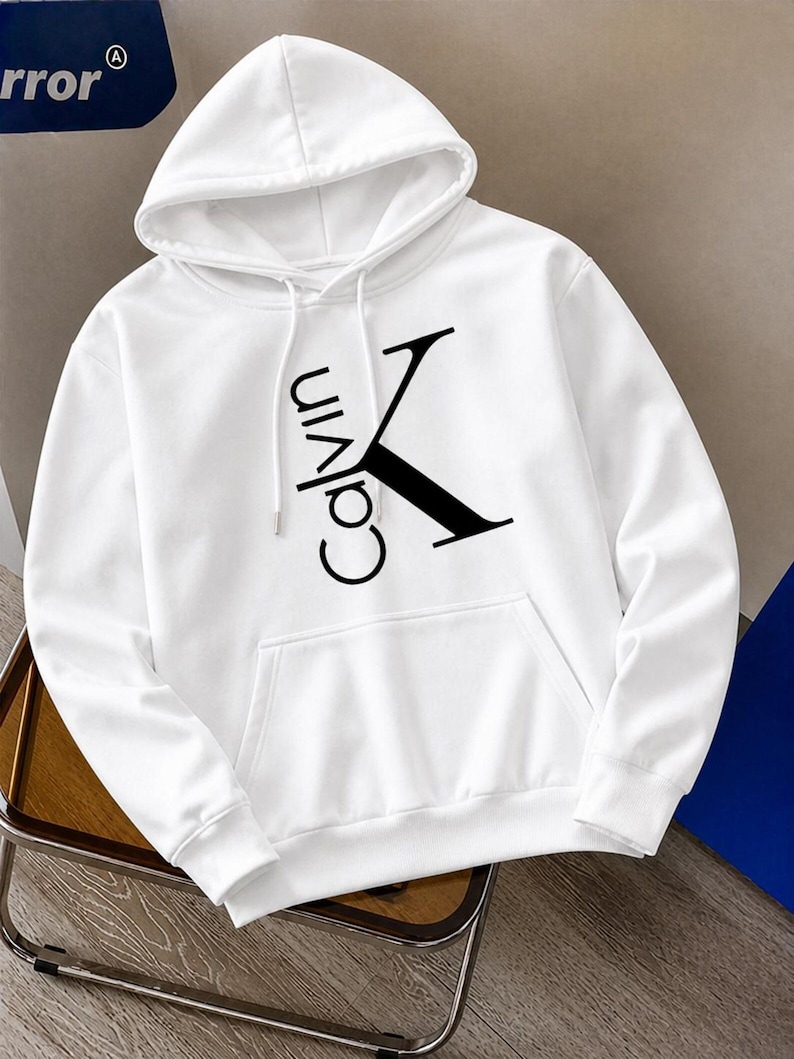 May include: White hooded sweatshirt with a front pocket and drawstring. The sweatshirt features the black text "Calvin K" on the front. The hoodie is made of a soft material.