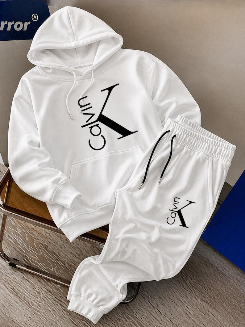 May include: White hoodie and sweatpants set. The hoodie features a drawstring hood and a front pocket. The set has the word "Calvin" and a "K" logo in black. The sweatpants have an elastic waistband and drawstring.