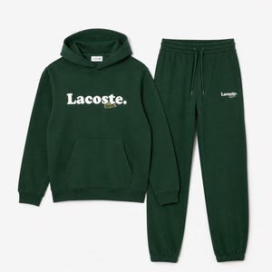 May include: A dark green hoodie and matching sweatpants set. The hoodie has a front pocket and the word "Lacoste" in white block letters across the chest, with a small crocodile logo. The sweatpants have a drawstring waist and the Lacoste logo.