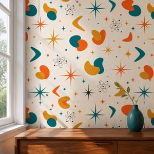 May include: Wallpaper featuring a repeating pattern of teal, orange, and yellow organic shapes, multi-pointed stars, and black line-drawn atom symbols on a cream background. A teal vase sits on a wooden surface in the foreground.