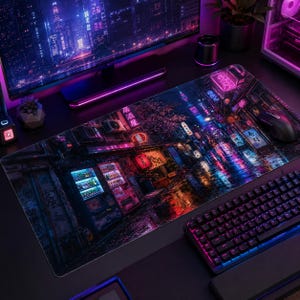 May include: A rectangular desk mat featuring a vibrant, detailed illustration of a rain-slicked city street at night. The scene is illuminated by glowing neon signs in pink, blue, and orange, with Japanese text visible on storefronts and vending machines.