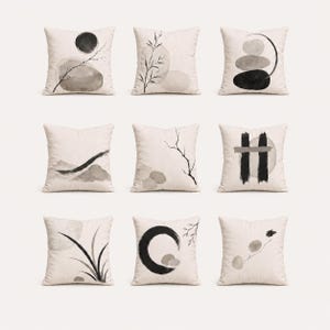 May include: A set of nine square scatter cushions featuring off-white fabric with black and grey ink-wash style illustrations. Designs include abstract circles, stacked stones, thin branches, bamboo-like leaves, and bold vertical brush strokes.