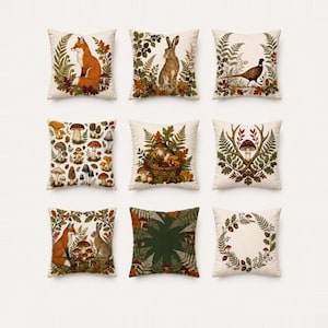 Op de afbeelding: Een set van negen vierkante sierkussens met diverse illustraties in een natuurthema. De ontwerpen bevatten een vos, een konijn, een fazant, diverse paddenstoelen, een mand met bosvruchten, een hertengewei en botanische kransen met varens.