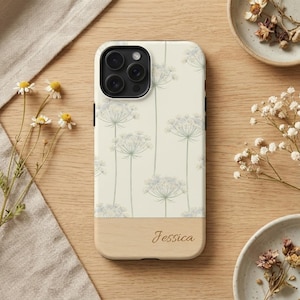 Può includere: Una custodia per telefono con un motivo floreale e una base in legno. La custodia presenta uno sfondo color crema con un motivo ripetuto di fiori bianchi e steli verdi. Il nome "Jessica" è inciso sulla base in legno.