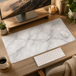 May include: A rectangular desk mat featuring a white and gray marble pattern. The mat has a smooth surface and rounded corners, providing a wide area for computer peripherals. The design mimics natural stone veining in shades of gray.