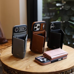 May include: A collection of leather phone cases with integrated wallet features. The cases are in various colors, including gray, brown, black, and pink. The cases are displayed on a wooden table, showcasing their design and functionality.
