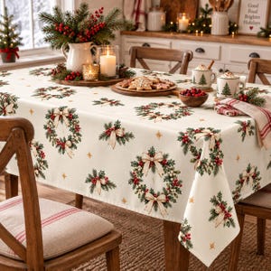 Puede incluir: Un mantel rectangular de color crema con un patrón repetitivo de coronas de pino verdes adornadas con bayas rojas y lazos beige, intercaladas con pequeñas estrellas doradas. La tela cubre una mesa de comedor preparada para una comida festiva.