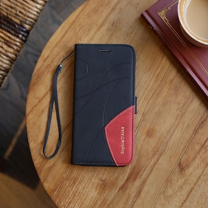 May include: Black and red phone case with a wrist strap. The case has a curved design on the black portion and a red accent with the name "Sophia Alex" printed on it. The case is on a wooden table.
