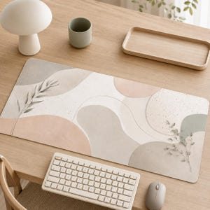 Könnte beinhalten: Eine rechteckige Schreibtischunterlage mit einem abstrakten Design aus weichen, gedeckten organischen Formen in Beige-, Salbeigrün- und Grautönen. Die Oberfläche weist eine gesprenkelte Textur und zarte botanische Illustrationen von Zweigen auf.