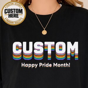 May include: Black sweatshirt with the word "CUSTOM" in white with rainbow layering. Below, the text reads "Happy Pride Month!" A circular logo at the top left says "CUSTOM DESIGN" and "CUSTOM HERE" with "PREMIUM QUALITY" around the edge.
