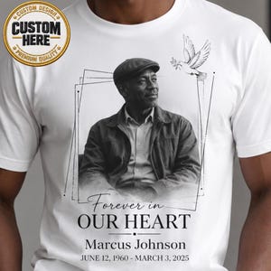 May include: White t-shirt featuring a black and white portrait of a man, a dove graphic, and the text "Forever in Our Heart." The shirt also includes the name "Marcus Johnson" and dates "June 12, 1960 - March 3, 2025."