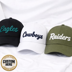 May include: Three baseball caps in black, white, and olive green. Each cap features embroidered team names: "Eagles" in teal, "Cowboys" in navy, and "Raiders" in white. A circular emblem with the text "CUSTOM HERE" is visible.