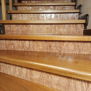 Puede incluir: Escalera de madera con escalones y contrahuellas marrones. Las contrahuellas presentan un diseño de azulejos texturizados y estampados en tonos marrones y beige. Los escalones son de madera pulida y la escalera tiene una barandilla de madera.